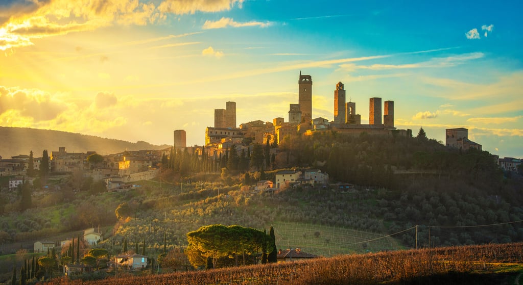 San Gimignano town skyline and medieval towers sunset. Italian olive trees in foreground. Tuscany, Italy, Europe.