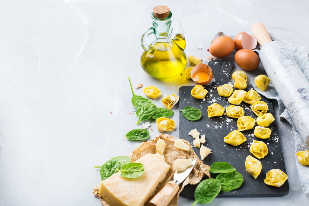 Assortment of italian food and ingredients, handmade tortellini with green spinach and cheese on a cutting board on a kitchen table. Copy space background