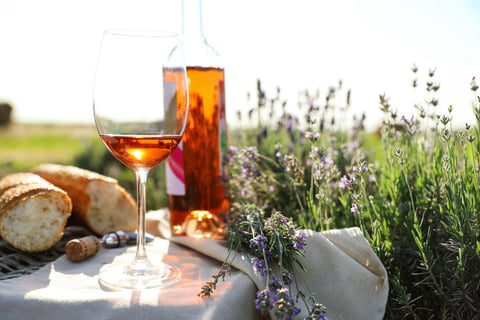 Composition with glass of wine on wicker table in lavender field. Space for text