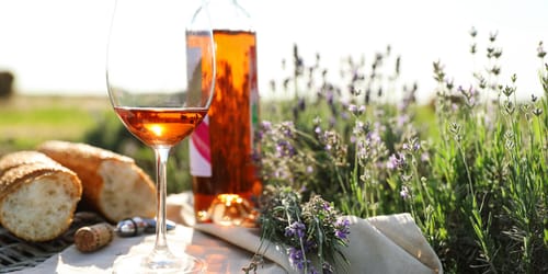 Composition with glass of wine on wicker table in lavender field. Space for text
