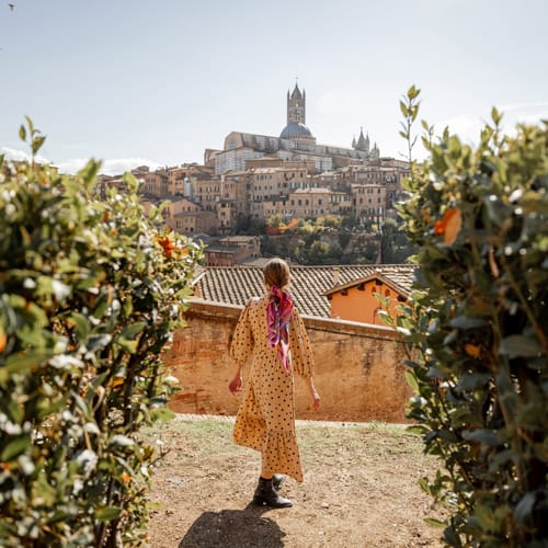 Stylish woman walks on background of cityscape of Siena old town. Concept of travel famous cities in Tosacny region of Italy