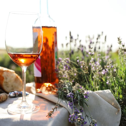 Composition with glass of wine on wicker table in lavender field. Space for text